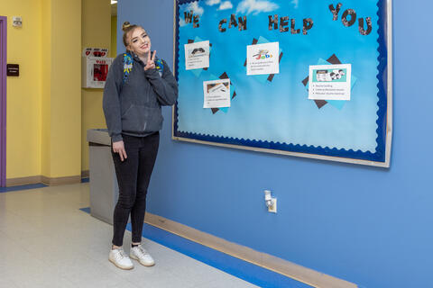At Eastlake High School, a happy student poses with peace fingers in front of a bulletin board that says “We Can Help You.”