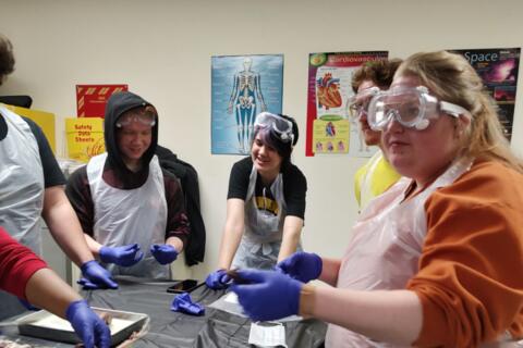 Eastlake High School students wear safety goggles, purple gloves, and white aprons while dissecting specimens in Biology.