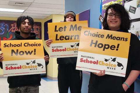 Three students at Eastlake High School hold yellow and white signs with a variety of school choice slogans such as “school choice now.”