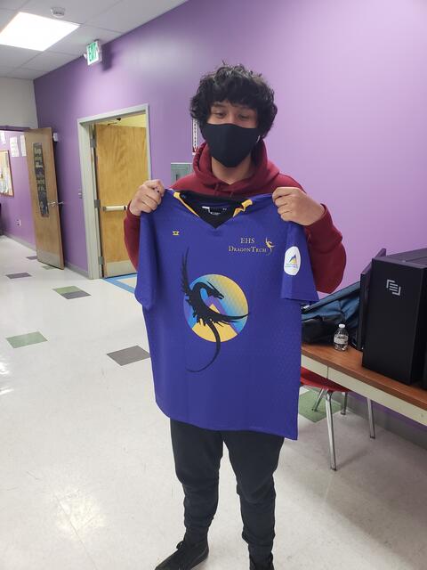 An Eastlake High School student holds up a jersey for the eSports team. The jersey is purple with the Eastlake mountain logo and a black dragon.