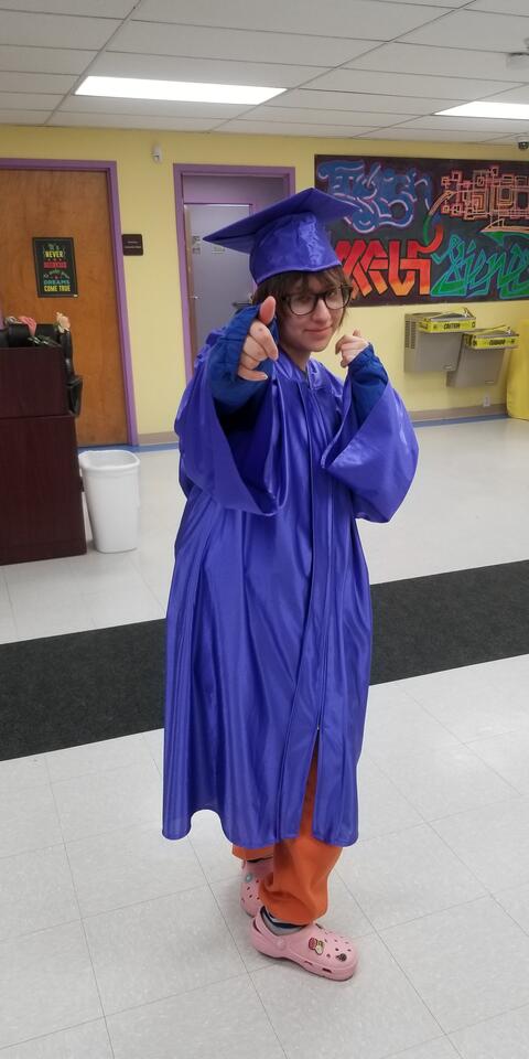 A graduate of Eastlake High School poses in the hallway of the school wearing a purple graduation cap and gown.