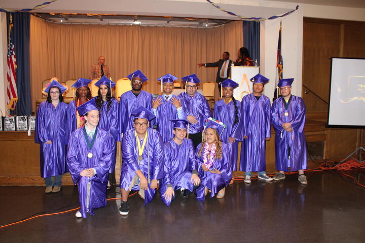 Eastlake High School students pose together for a photo during graduation. The students are wearing brilliant purple caps and gowns, as well as various awards, cords and medals. 