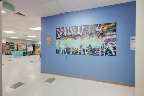 A large mural with student hands reaching out toward the text REACH hangs in front of a blue wall at Eastlake High School.